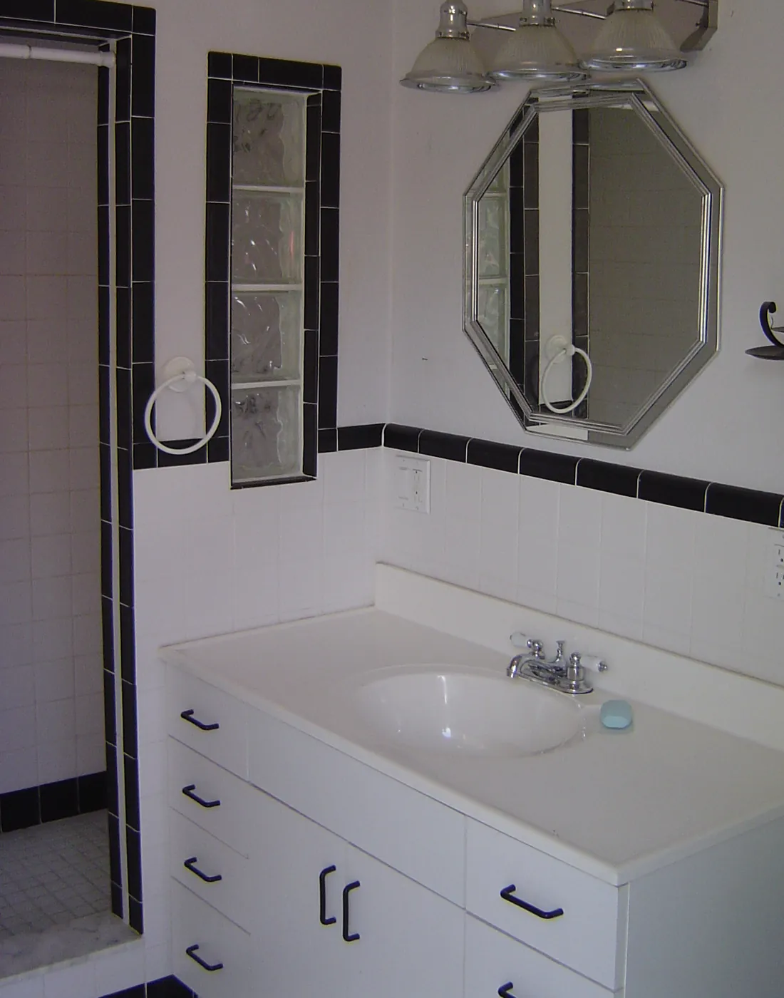 Finished bathroom vanity with framed mirror, chrome sconce lighting and black tile trim