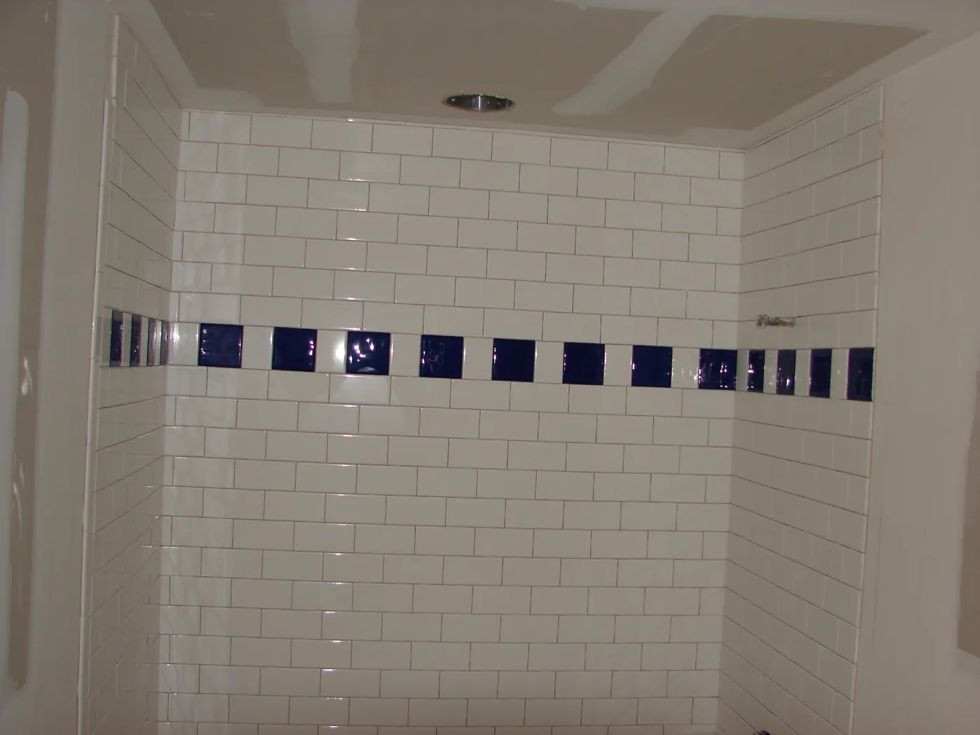 Tiled shower surround with a horizontal blue glass mosaic accent stripe