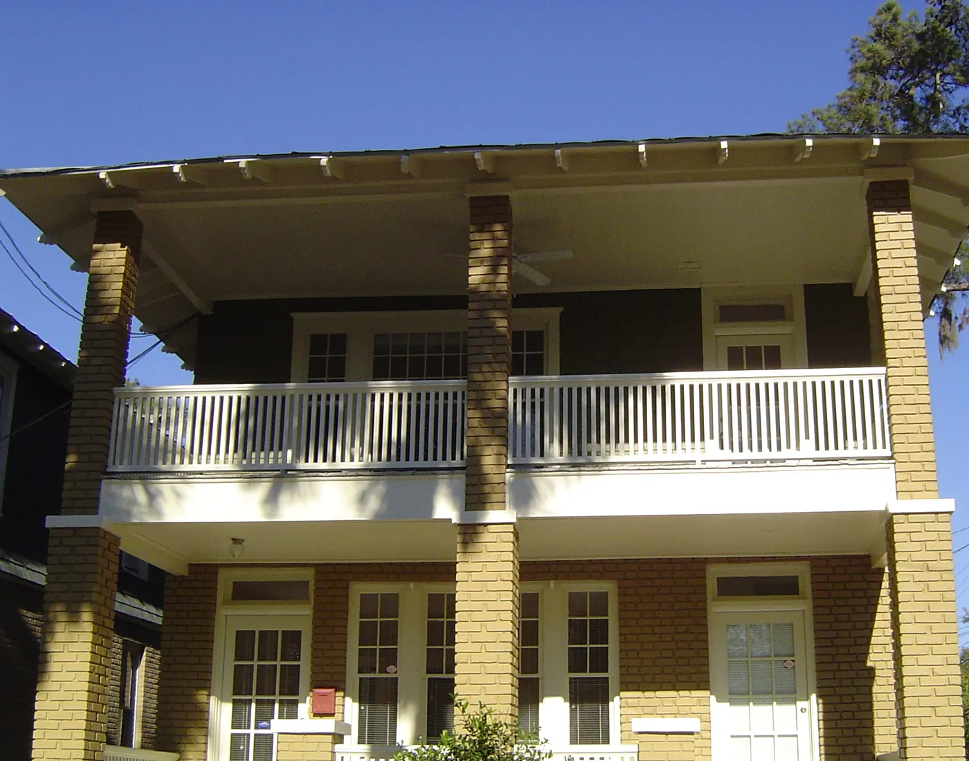 Two-story yellow craftsman home with double-stacked front porches and brick columns