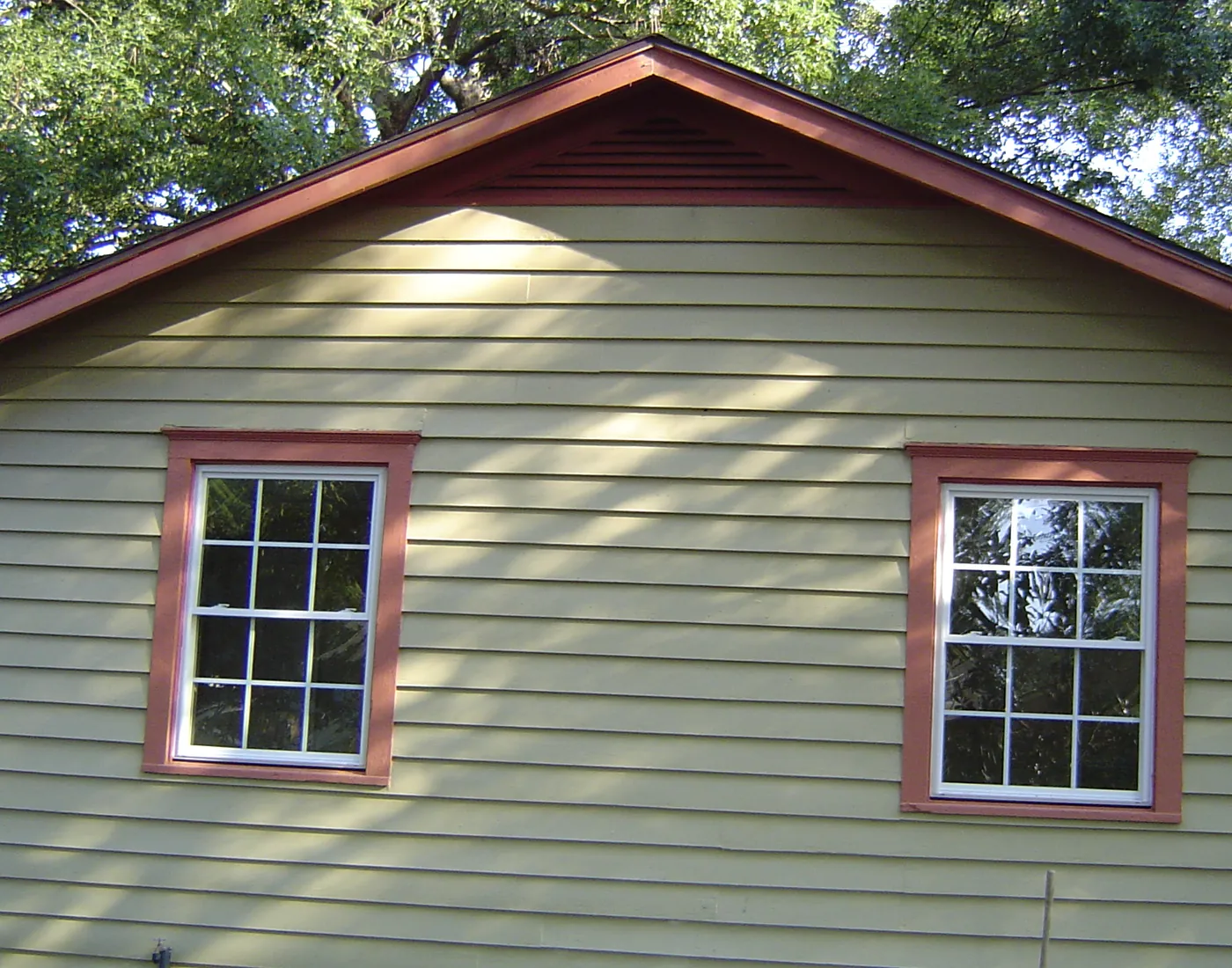 Green craftsman home exterior with red-trimmed double-hung windows and lap siding