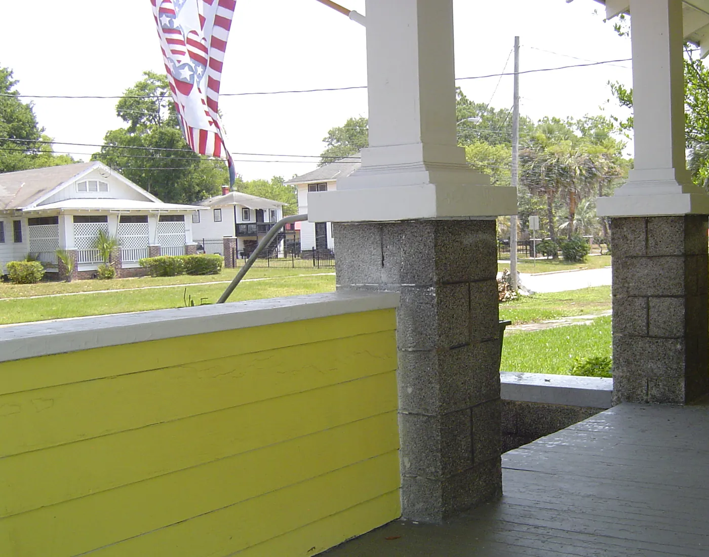 Freshly painted front porch with yellow siding, stucco columns and finished decking