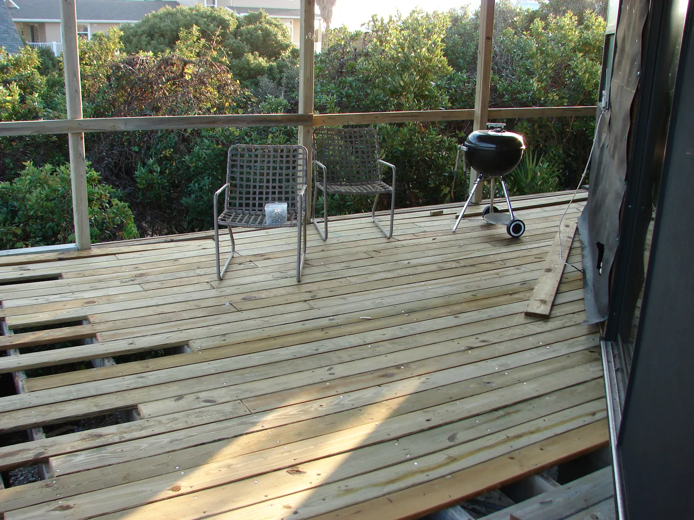 Finished screened porch with a fresh wood deck, patio chairs and a charcoal grill