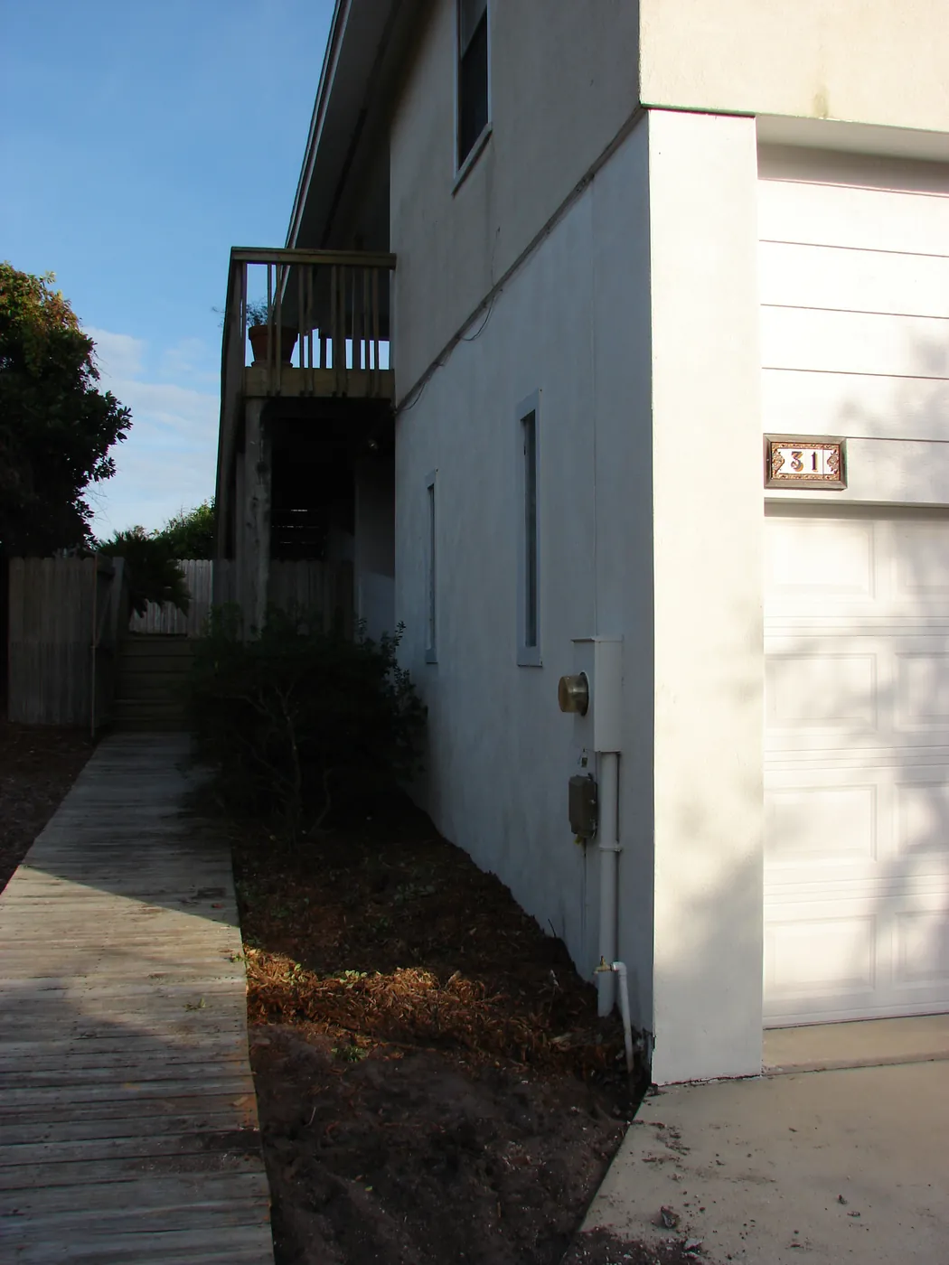 Side elevation of a white stucco home with a paved walkway leading to the back