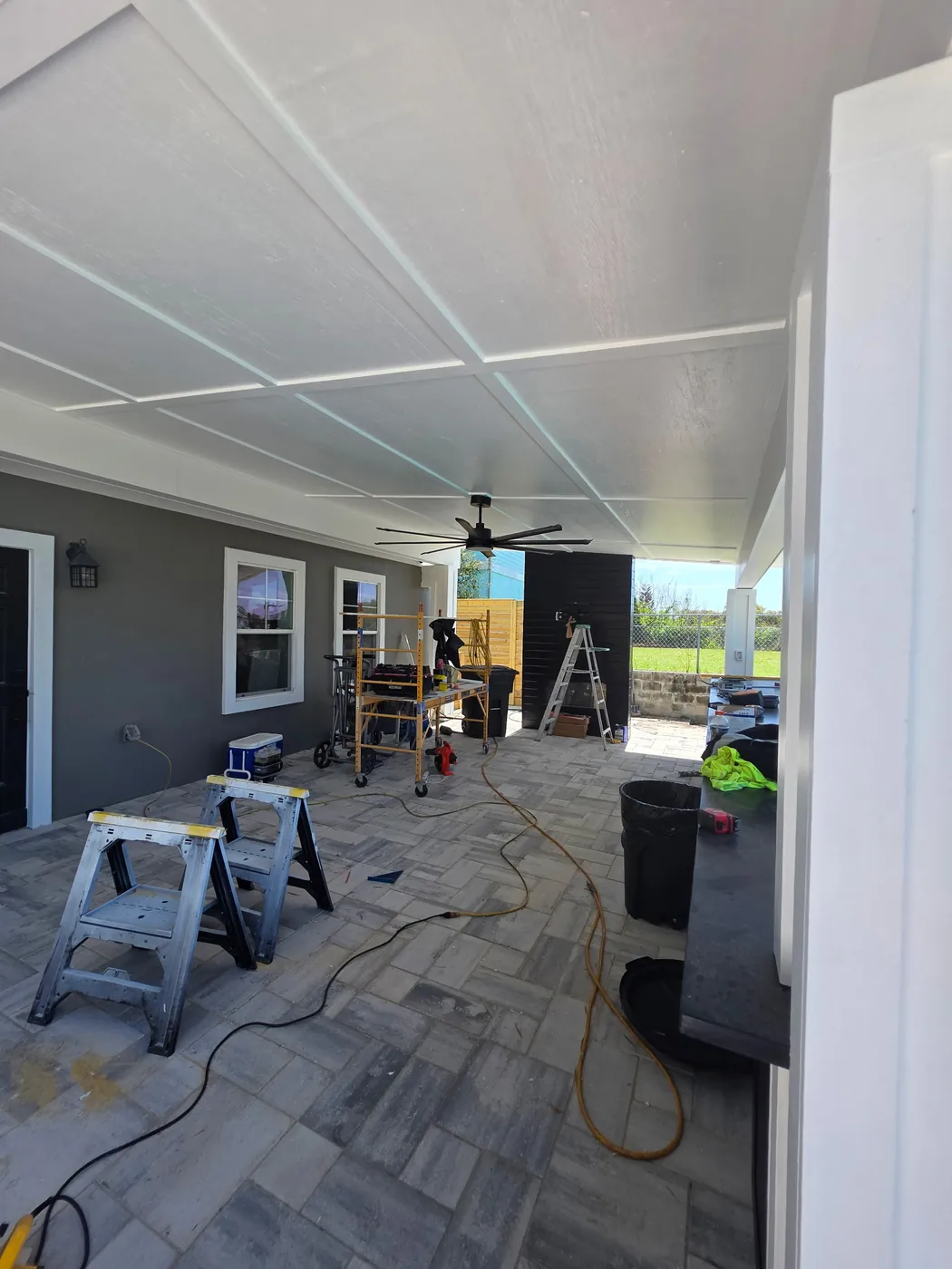Covered cabana during finish work with a paneled ceiling, ceiling fan, ladders and tools