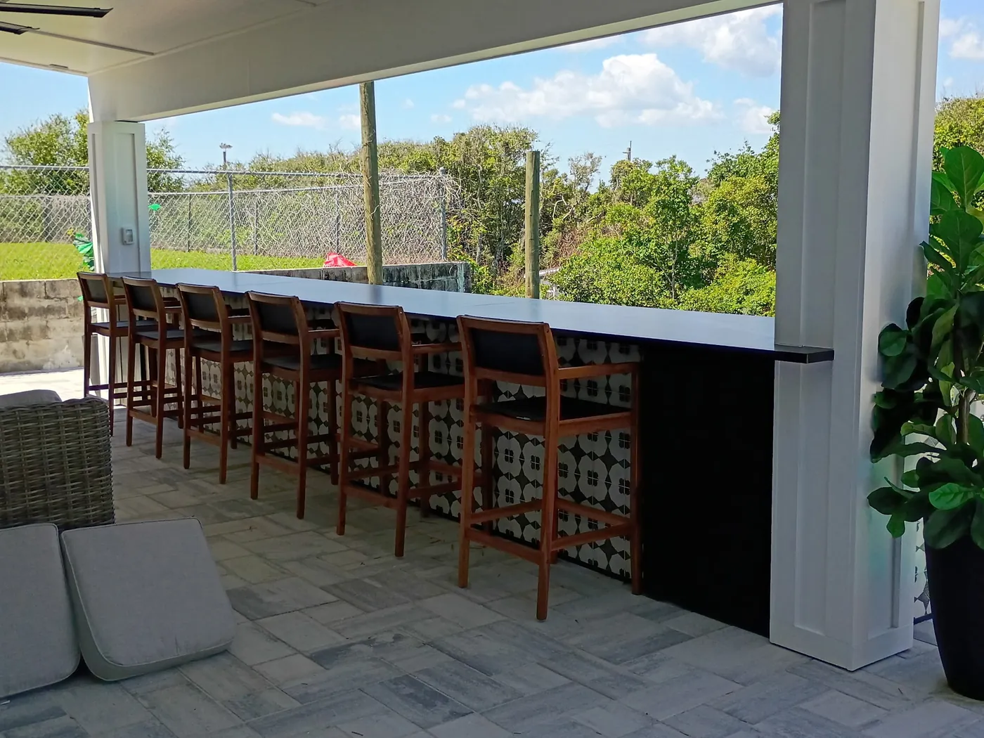 Finished outdoor bar with a black countertop, patterned face and a row of wood stools