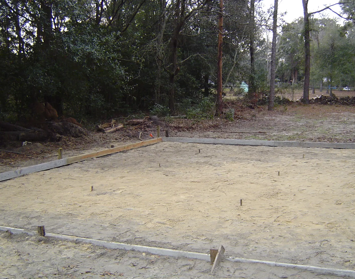 Wood-formed foundation footprint set on compacted sand, ready for a poured concrete slab