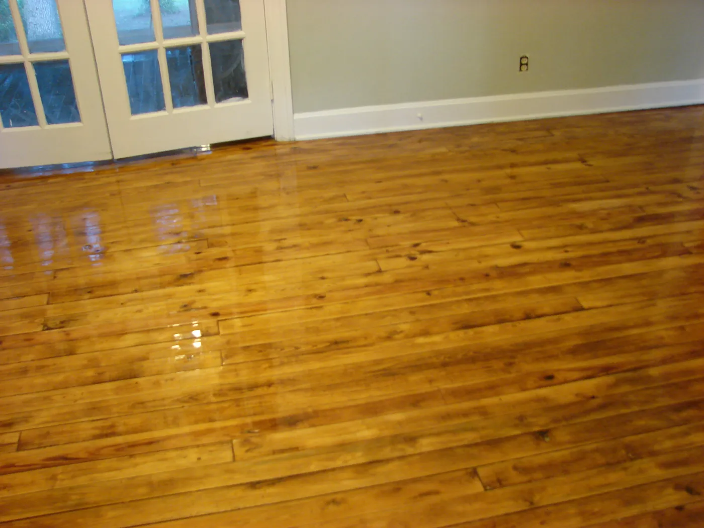 Newly refinished pine plank floor with a glossy finish beside a wood-framed French door