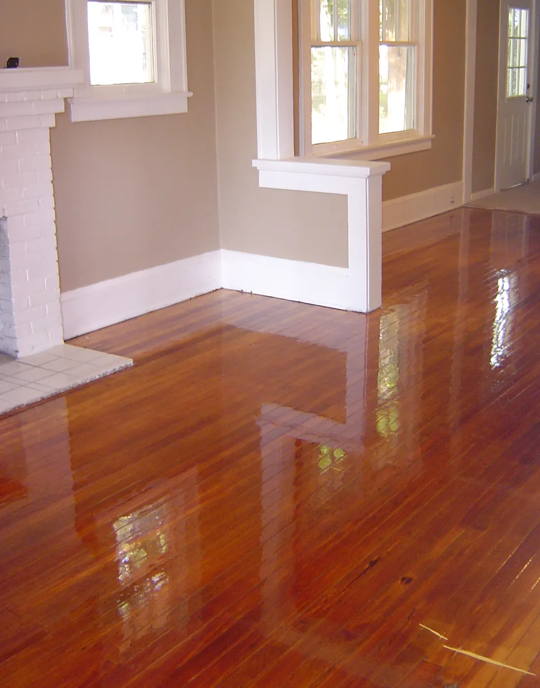 Glossy refinished hardwood floors in a bright room finished with white crown molding and baseboards