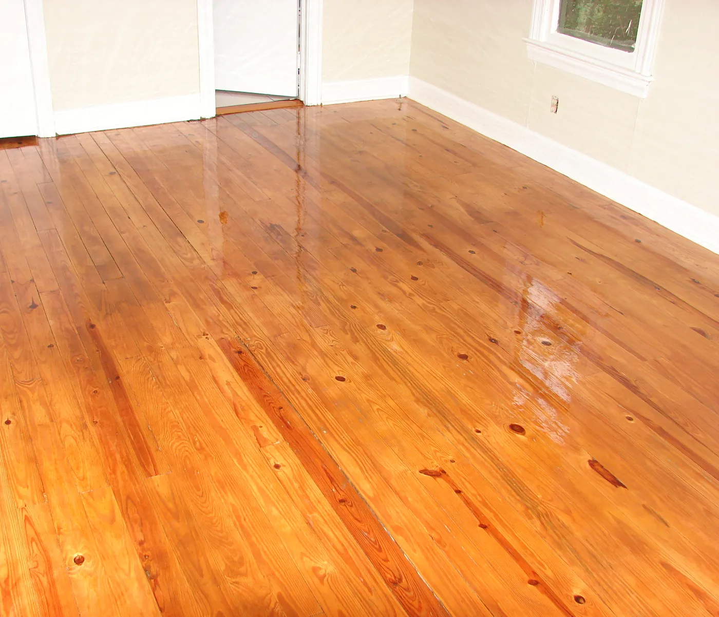 Refinished pine flooring in an empty room finished with white baseboard trim