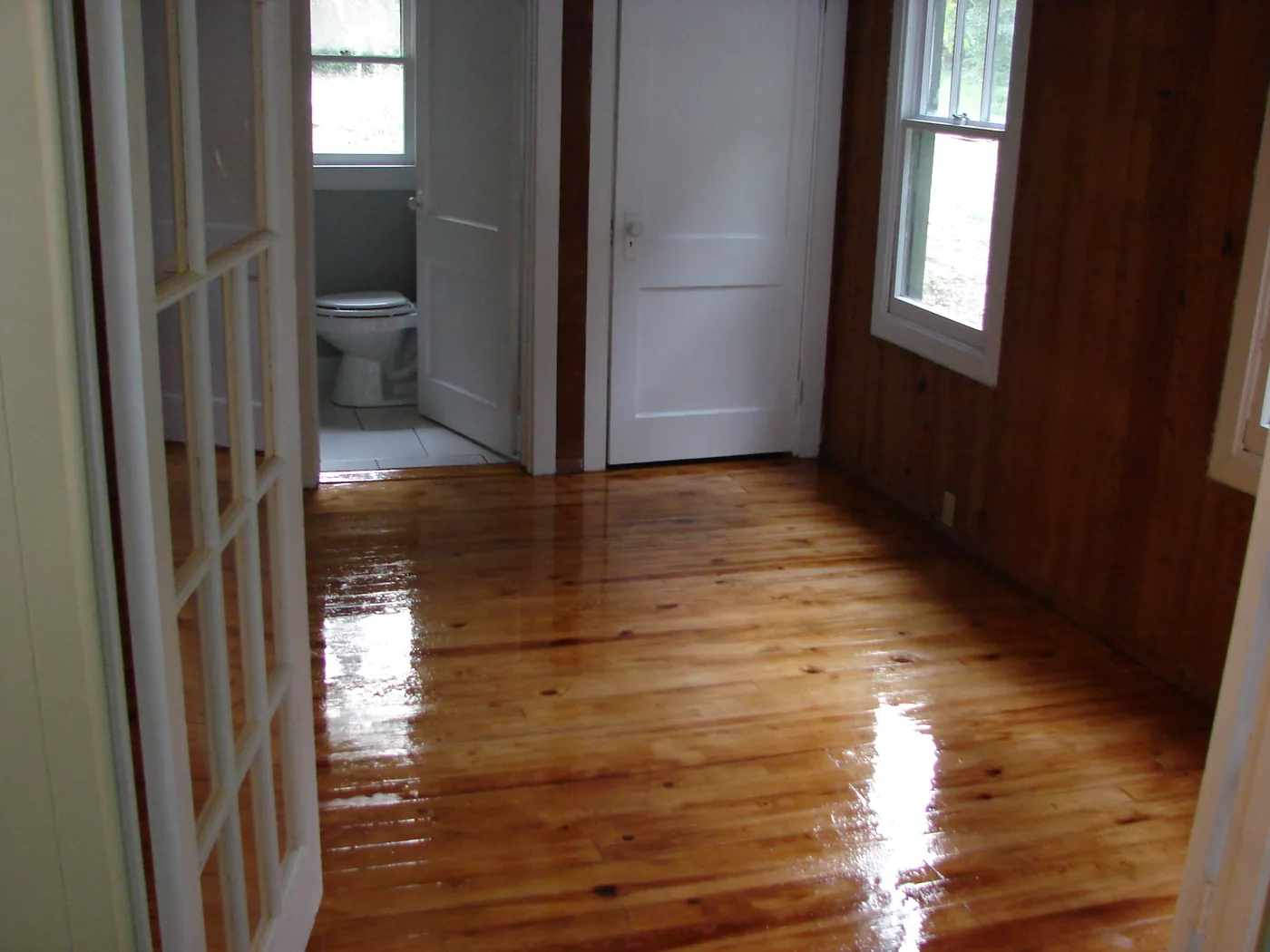 Refinished pine floors viewed through glass-paned wood French doors into an adjoining room