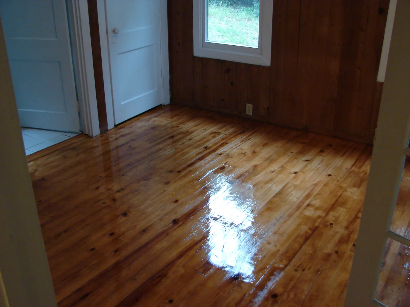 Refinished pine plank floor next to a natural wood-paneled wall and door