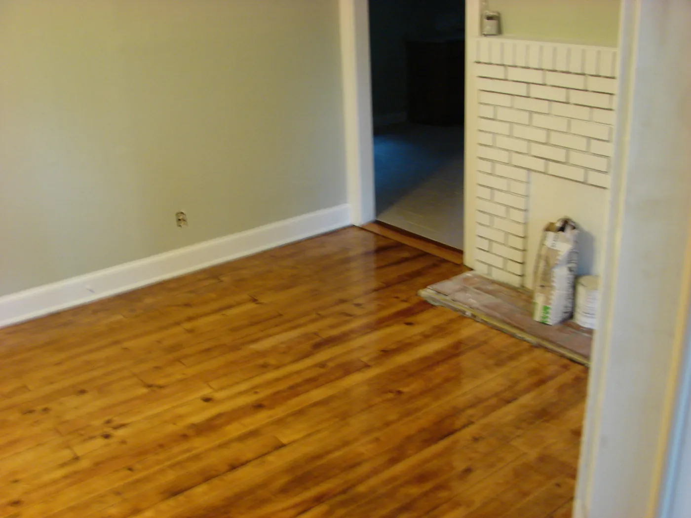 Refinished wood floor beside a painted white brick fireplace surround