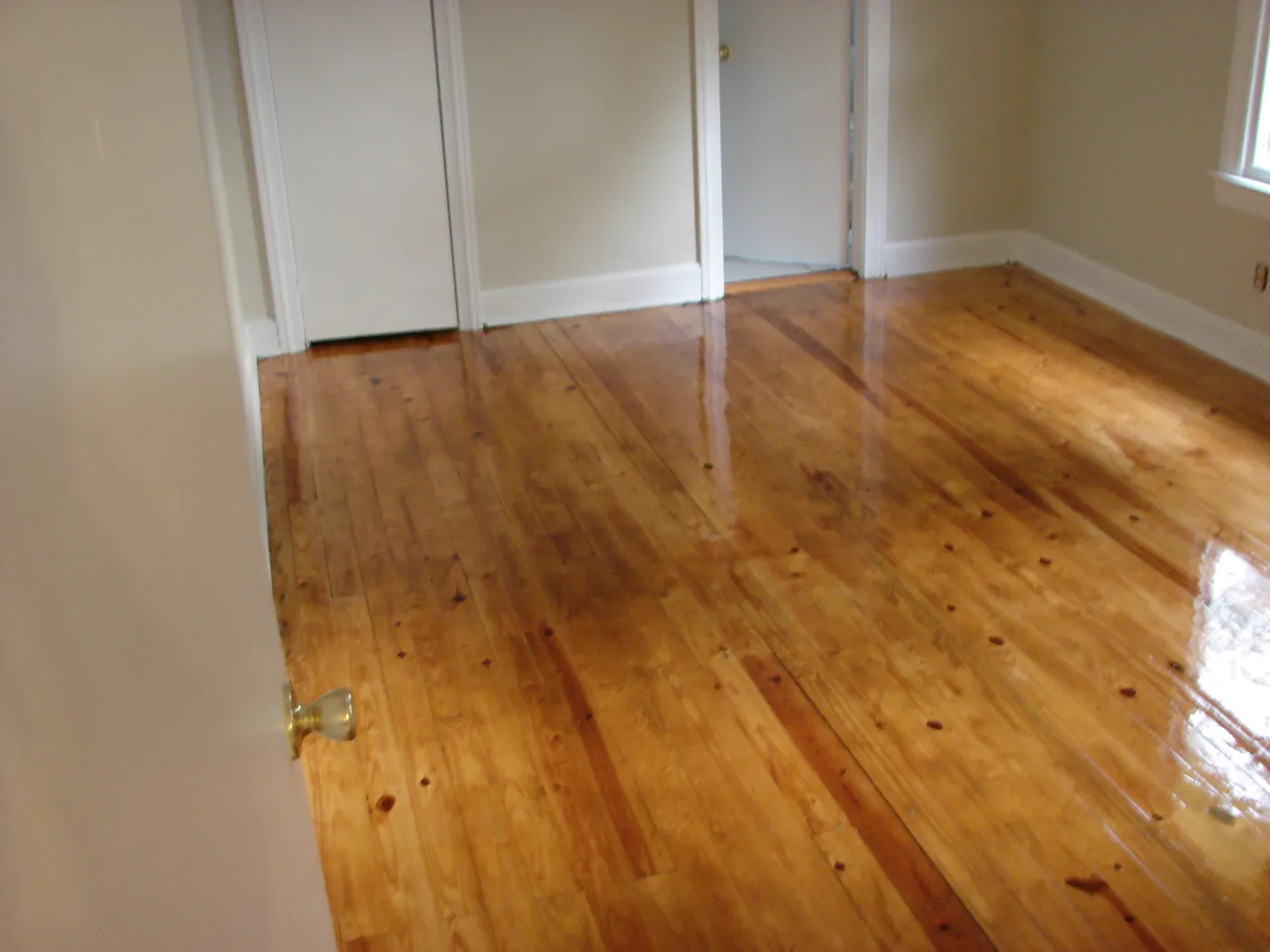 Freshly refinished pine floor with a wet-look sheen against white trimmed walls