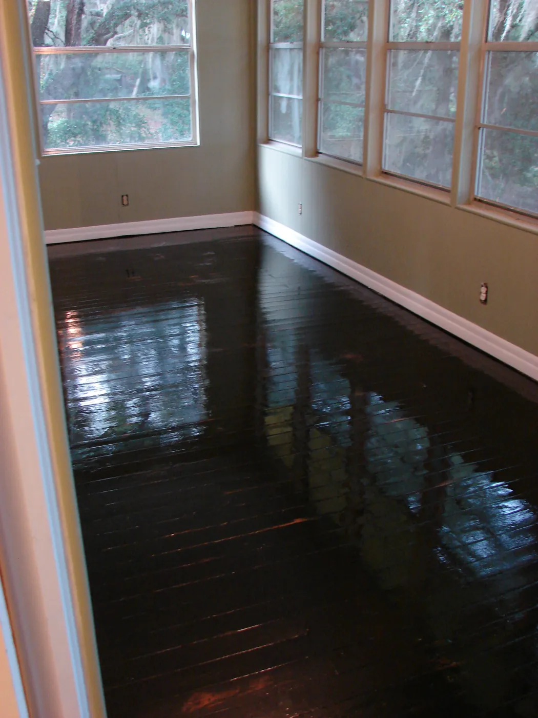 Dark refinished wood floor in a window-lined sunroom