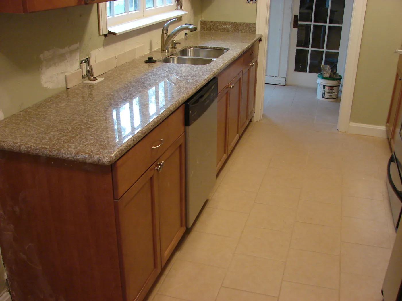 Kitchen counter run with beige granite countertop, stainless sink and dishwasher in wood cabinetry
