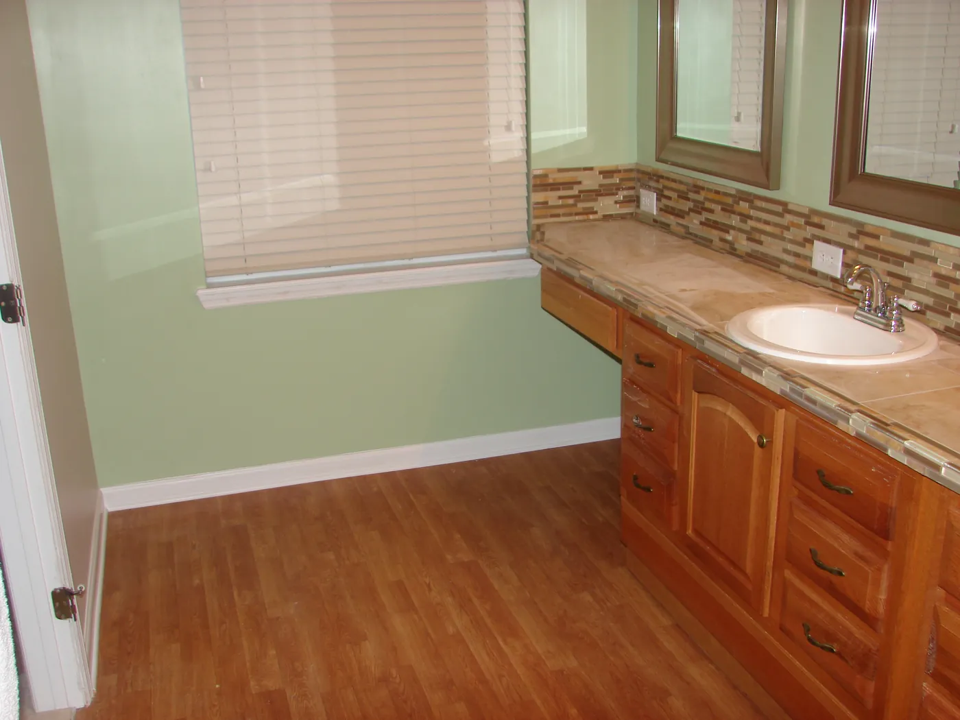 Bathroom double vanity with travertine stone countertop and glass mosaic backsplash beneath a window