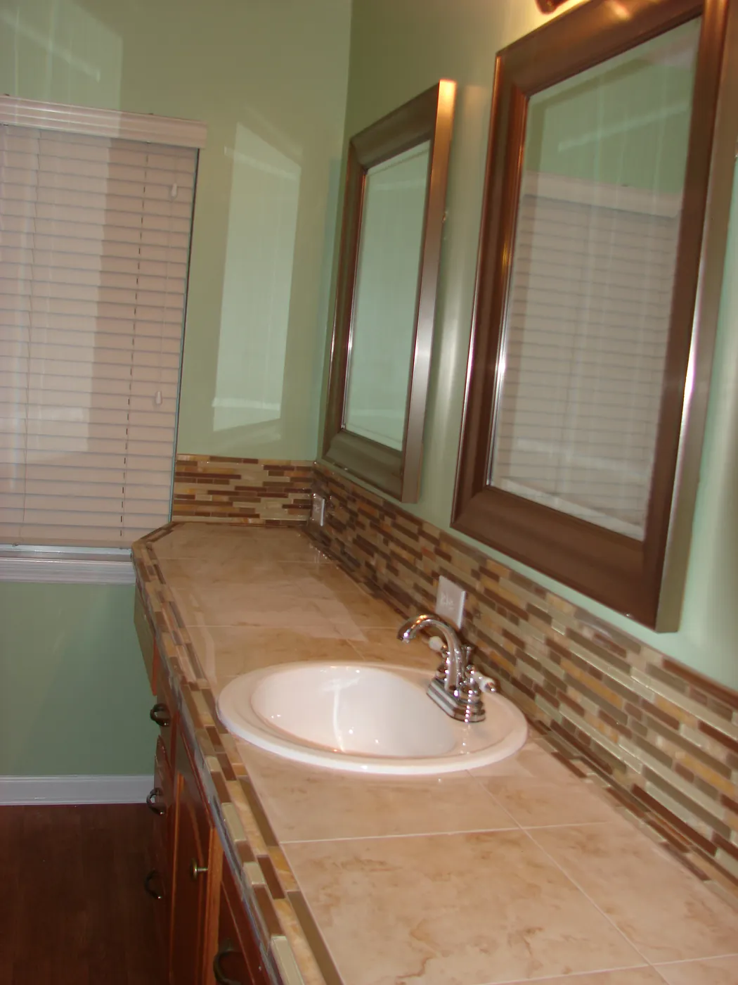 Double sink vanity topped with natural travertine stone counter and glass mosaic tile backsplash