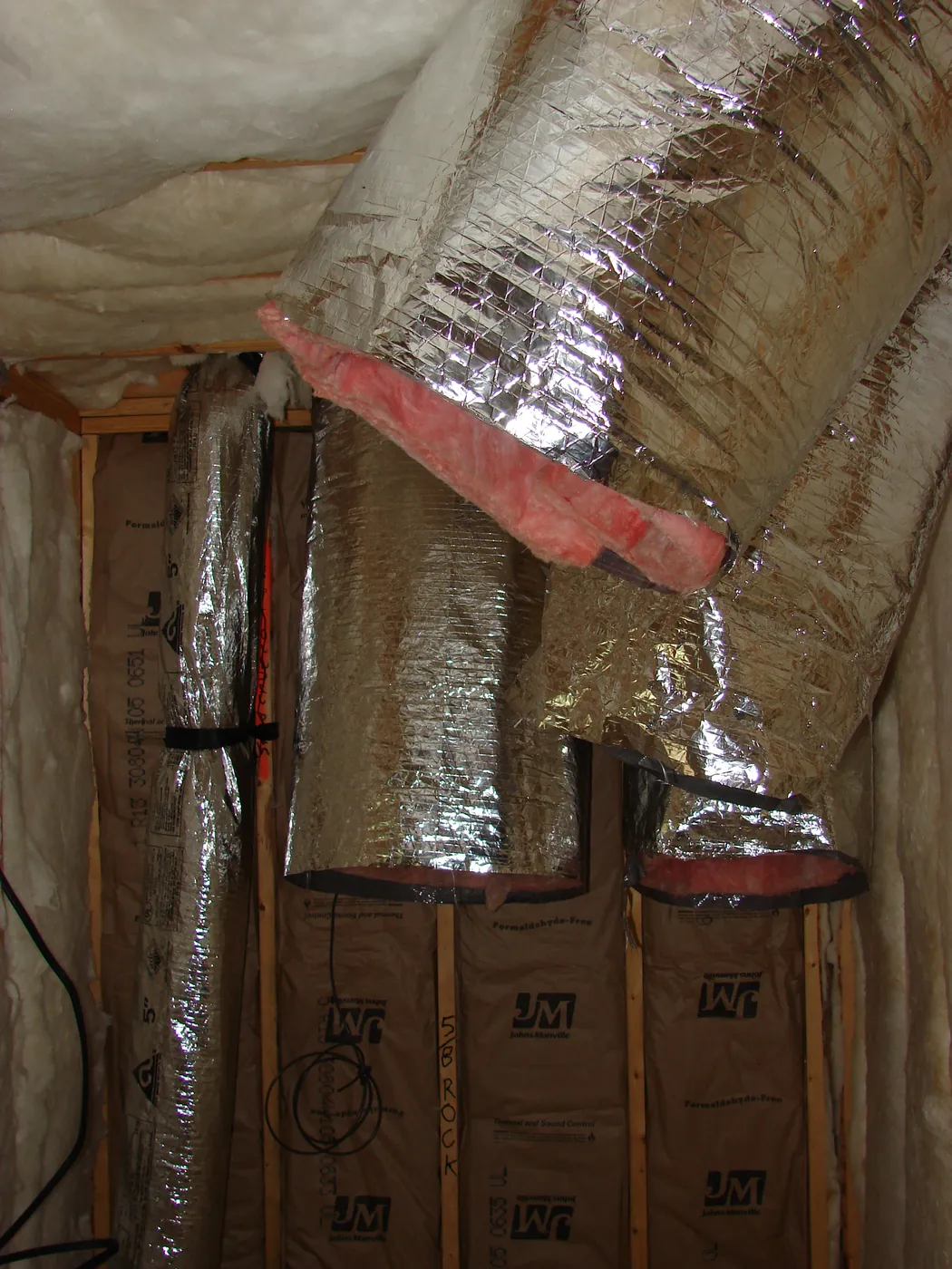 Insulated silver flex ductwork and HVAC trunk lines routed through an attic during a new-construction install