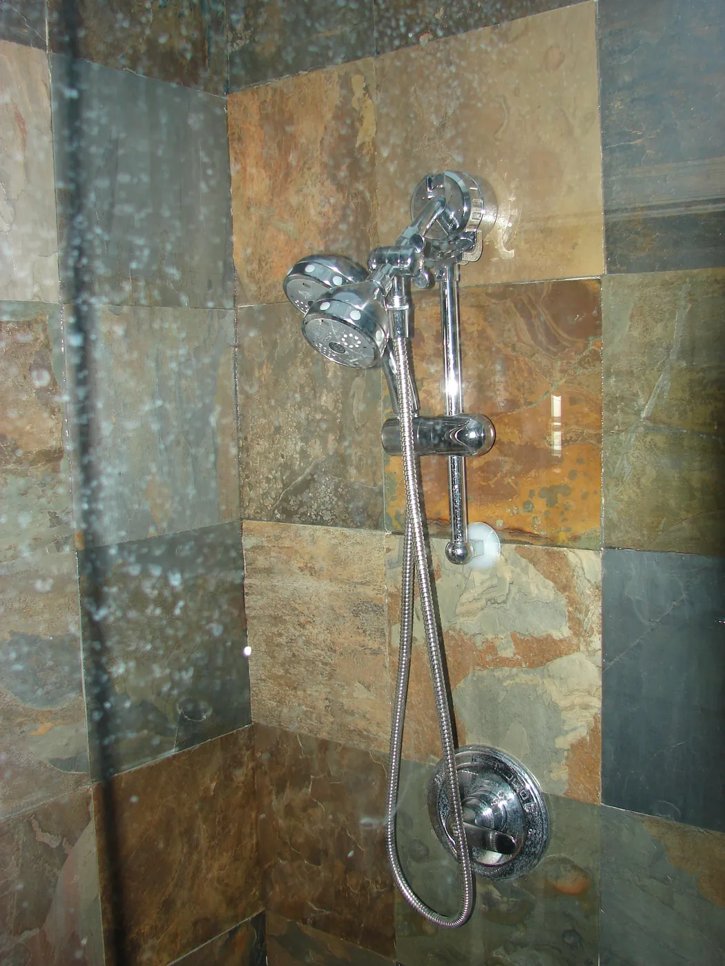 Walk-in shower clad in multicolor slate tile with chrome handheld and rain shower fixtures
