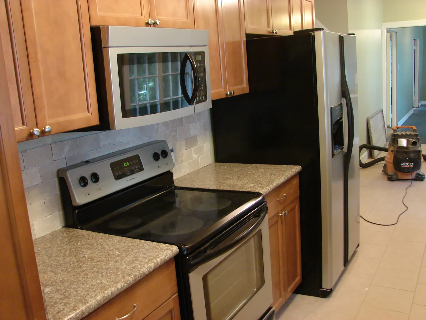 Kitchen appliance run with stainless microwave, electric range and refrigerator against tile backsplash and granite counters