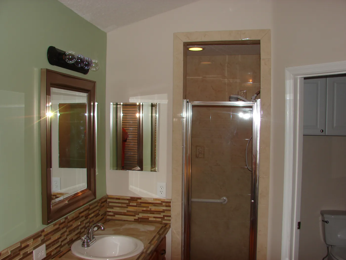Bathroom with glass-enclosed tile shower, framed mirror and mosaic tile accent over the vanity