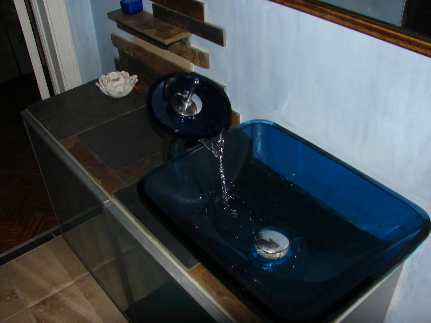 Blue glass vessel sink mounted on a floating vanity with running faucet detail
