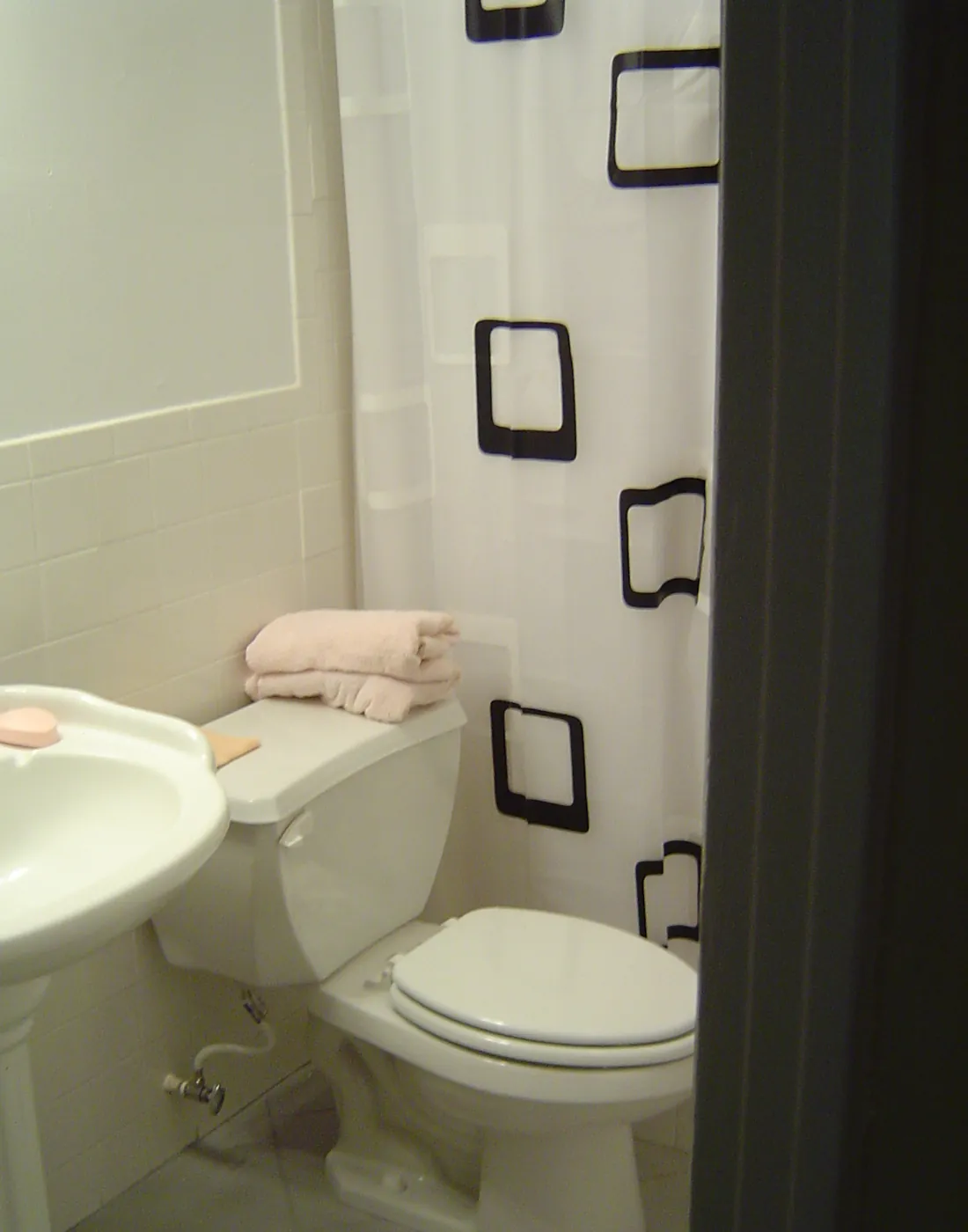 Finished guest bathroom with pedestal sink, toilet and tile tub surround with black accent decor