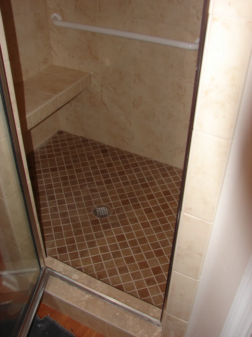 Travertine tile shower stall with glass door and mosaic accent trim