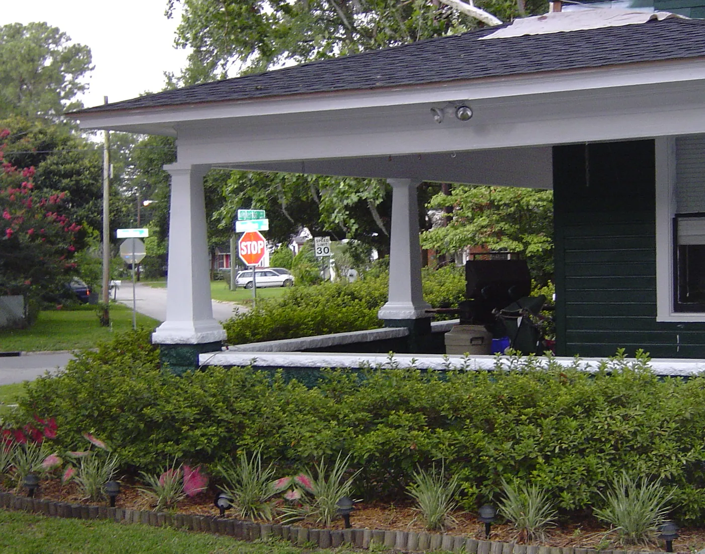 Green bungalow with layered foundation shrub beds and manicured lawn along the front walk