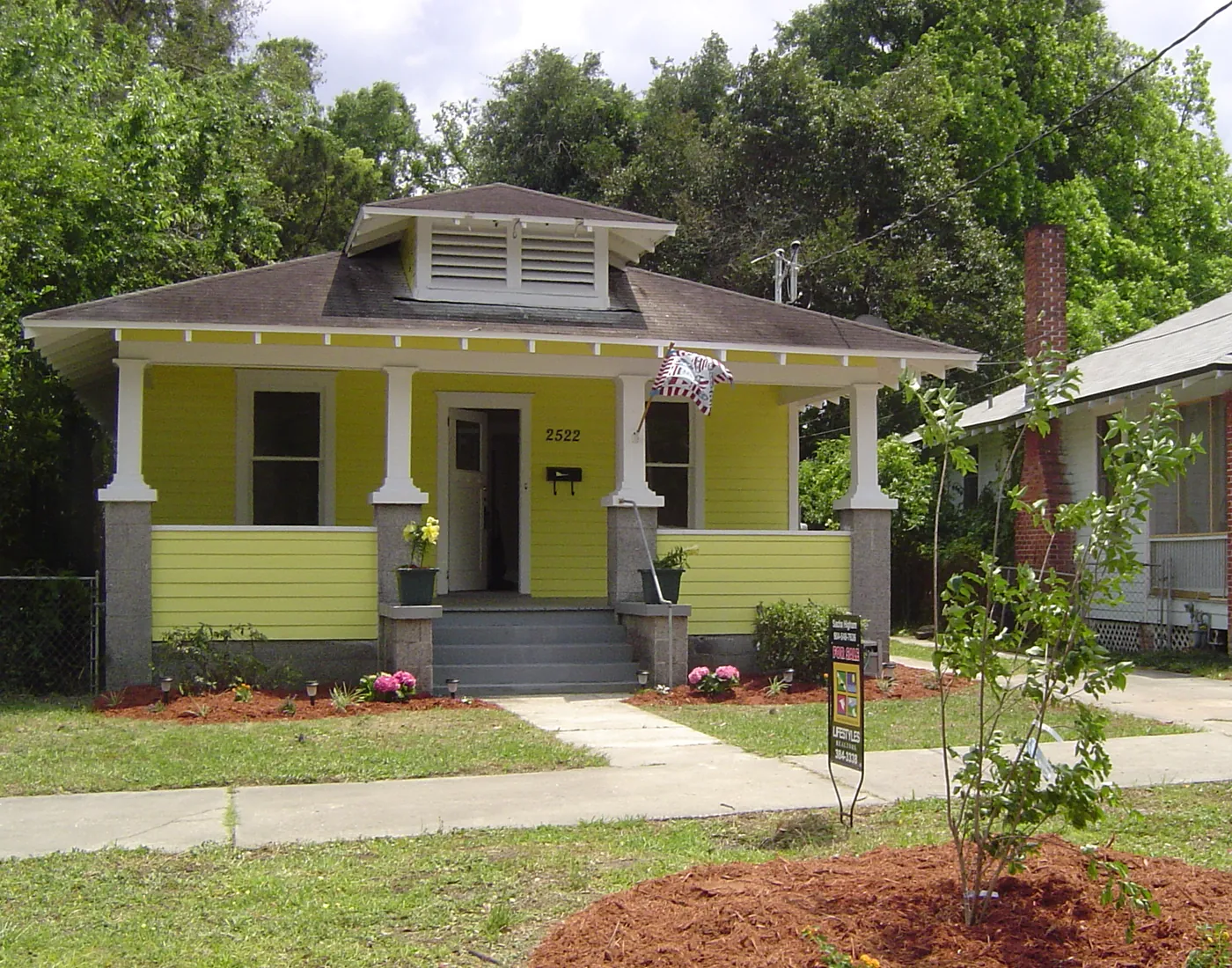 Yellow bungalow front yard with a mulched tree ring, young landscape tree and green sod