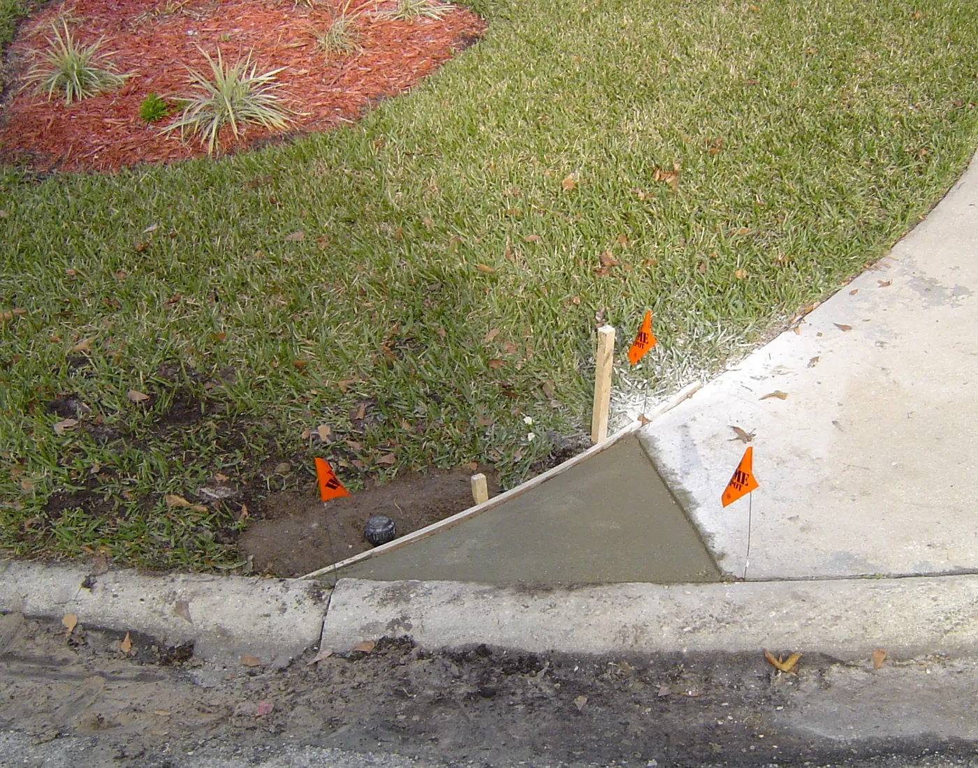 Newly installed lawn sprinkler head at a driveway edge with marking flags and fresh sod