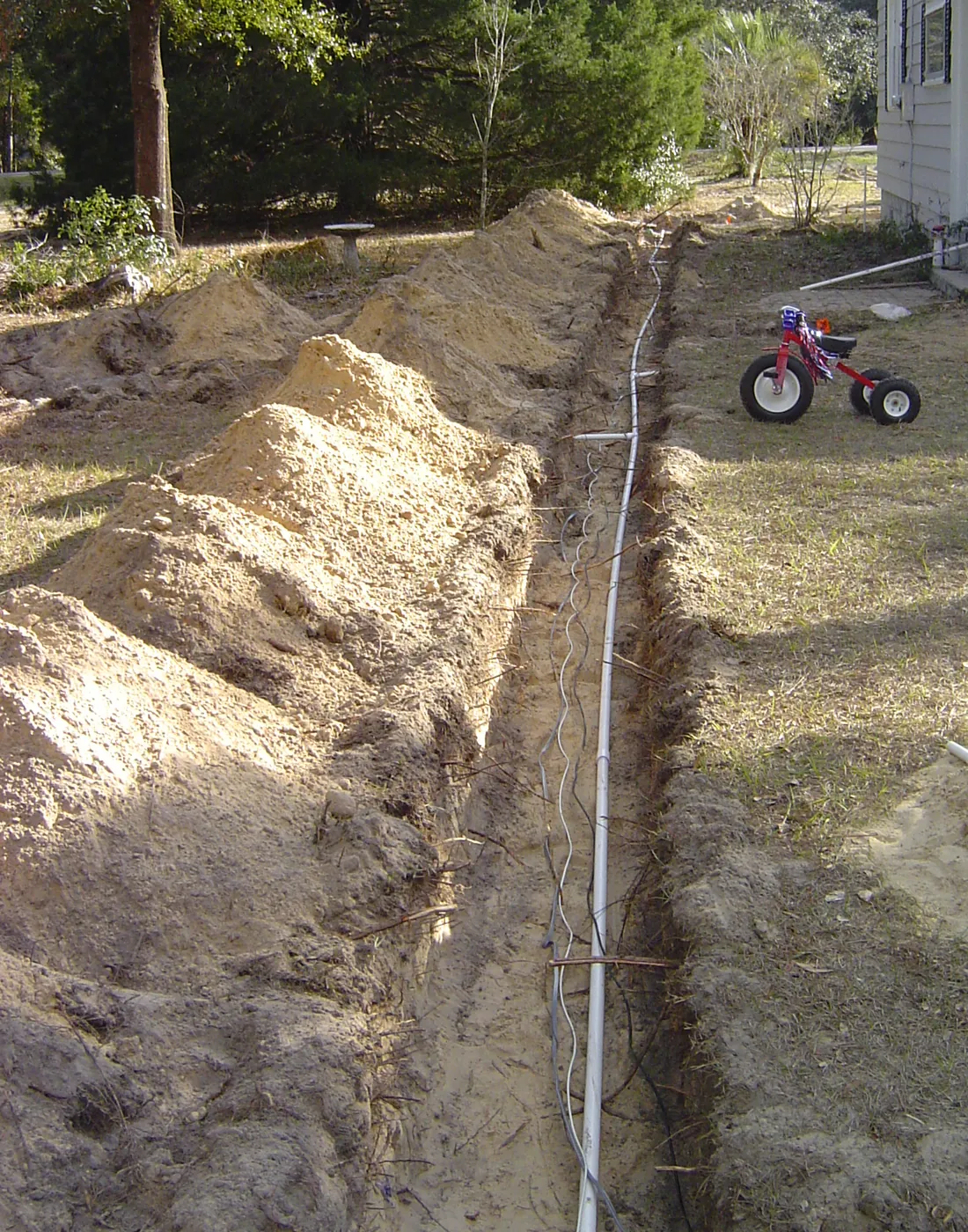 Open irrigation trench with new sprinkler supply line running across a graded backyard