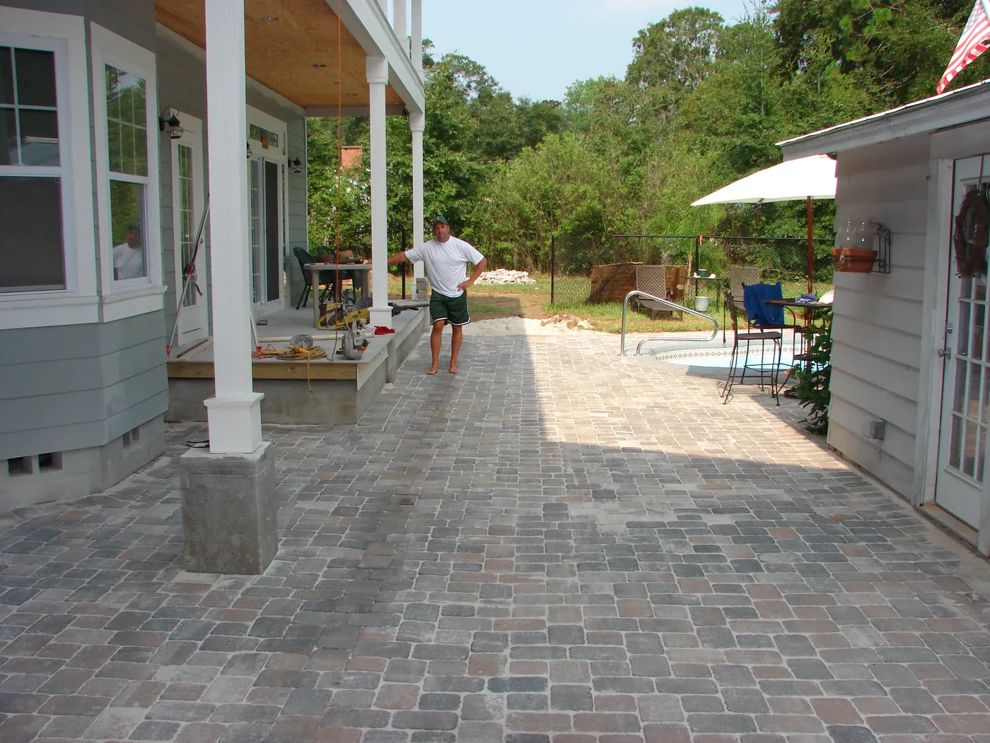 Interlocking brick paver patio running along a covered back porch with patio umbrella