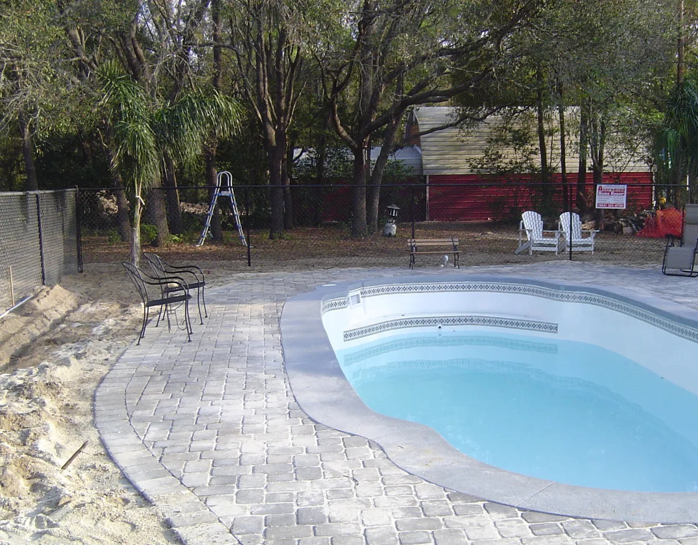 Freeform fiberglass pool surrounded by a herringbone brick paver pool deck