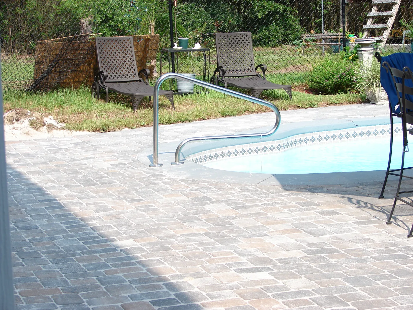 Backyard pool with a wide brick paver deck and poolside lounge chairs