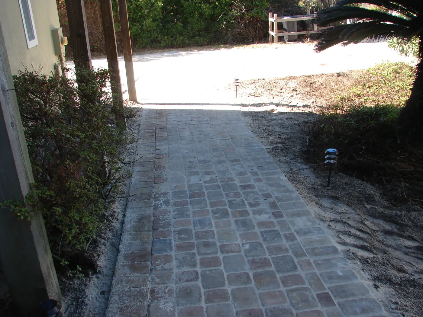Curved brick paver walkway winding through landscaping in a sunny backyard