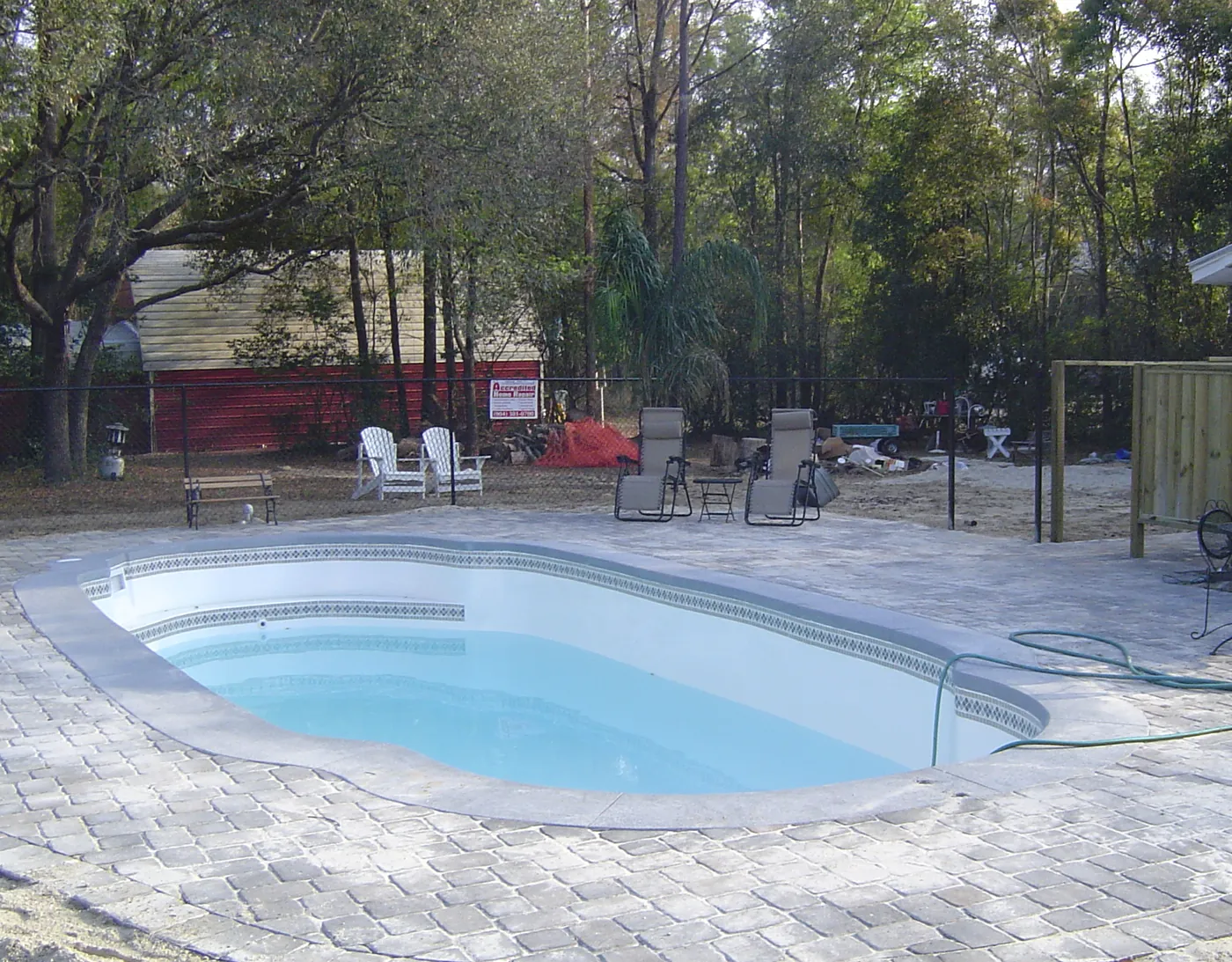 Freeform pool with a broad brick paver pool deck and patio seating area