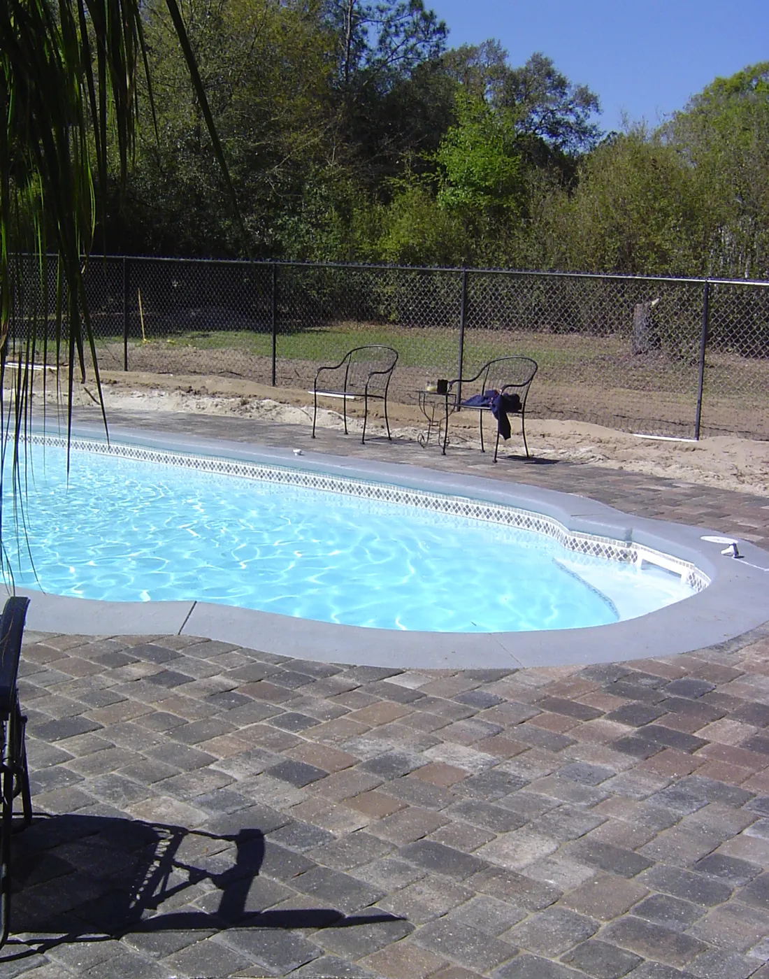 Poolside brick paver deck with lounge chair beside a fiberglass pool