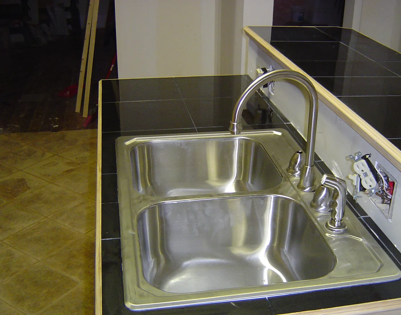 Close-up of a stainless steel double-basin kitchen sink with a chrome pull-neck faucet set into a dark tile countertop