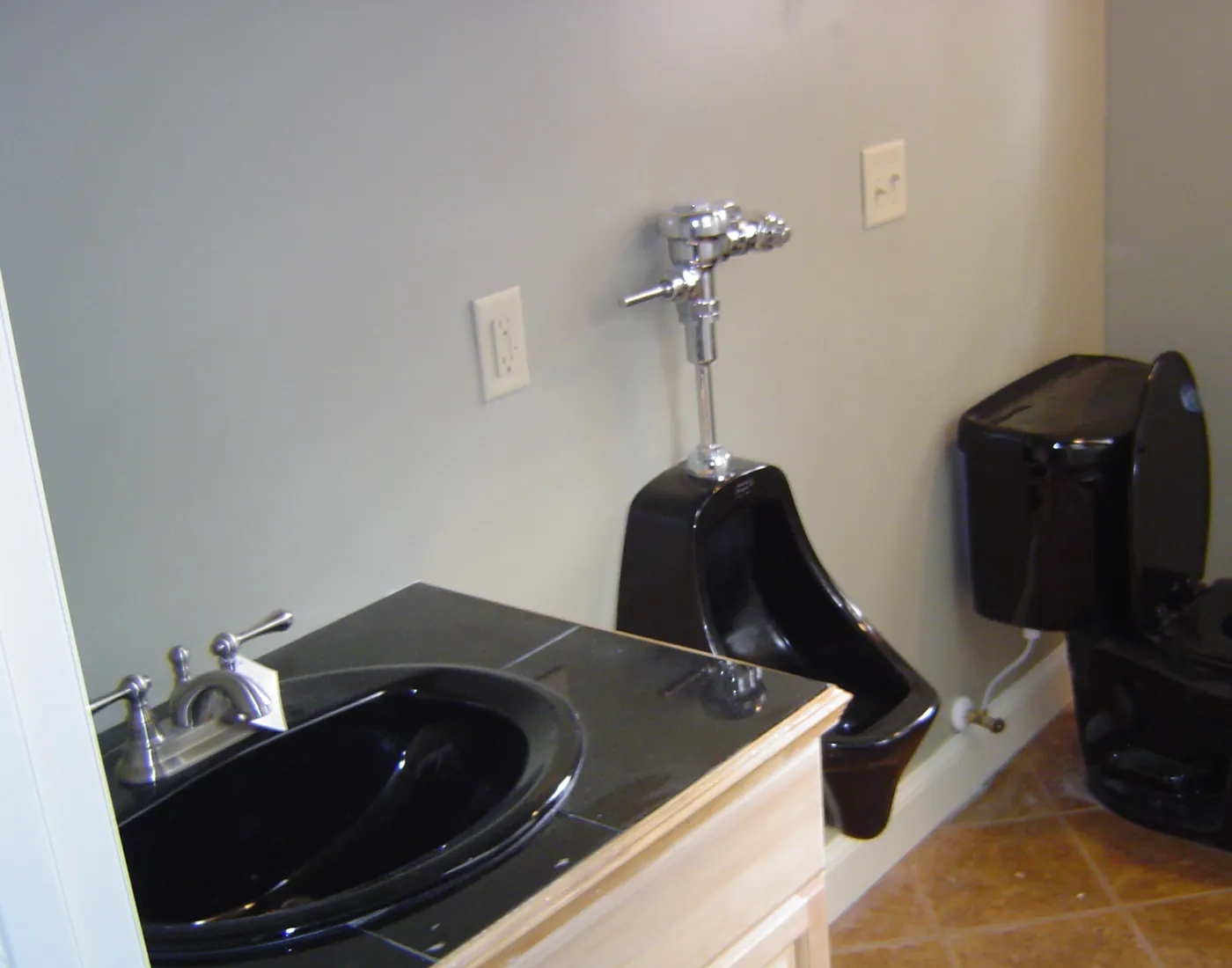 Black drop-in bathroom vanity sink with chrome faucet beside a matching black toilet on tile flooring