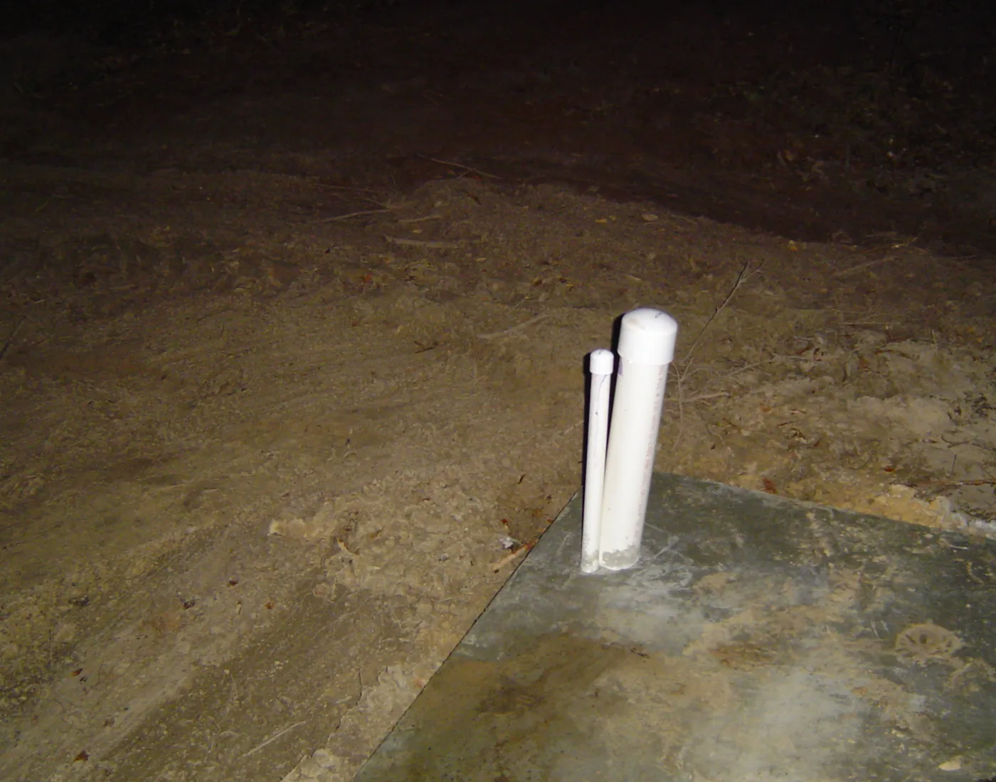 Capped white PVC plumbing stub-out rising from a poured concrete slab