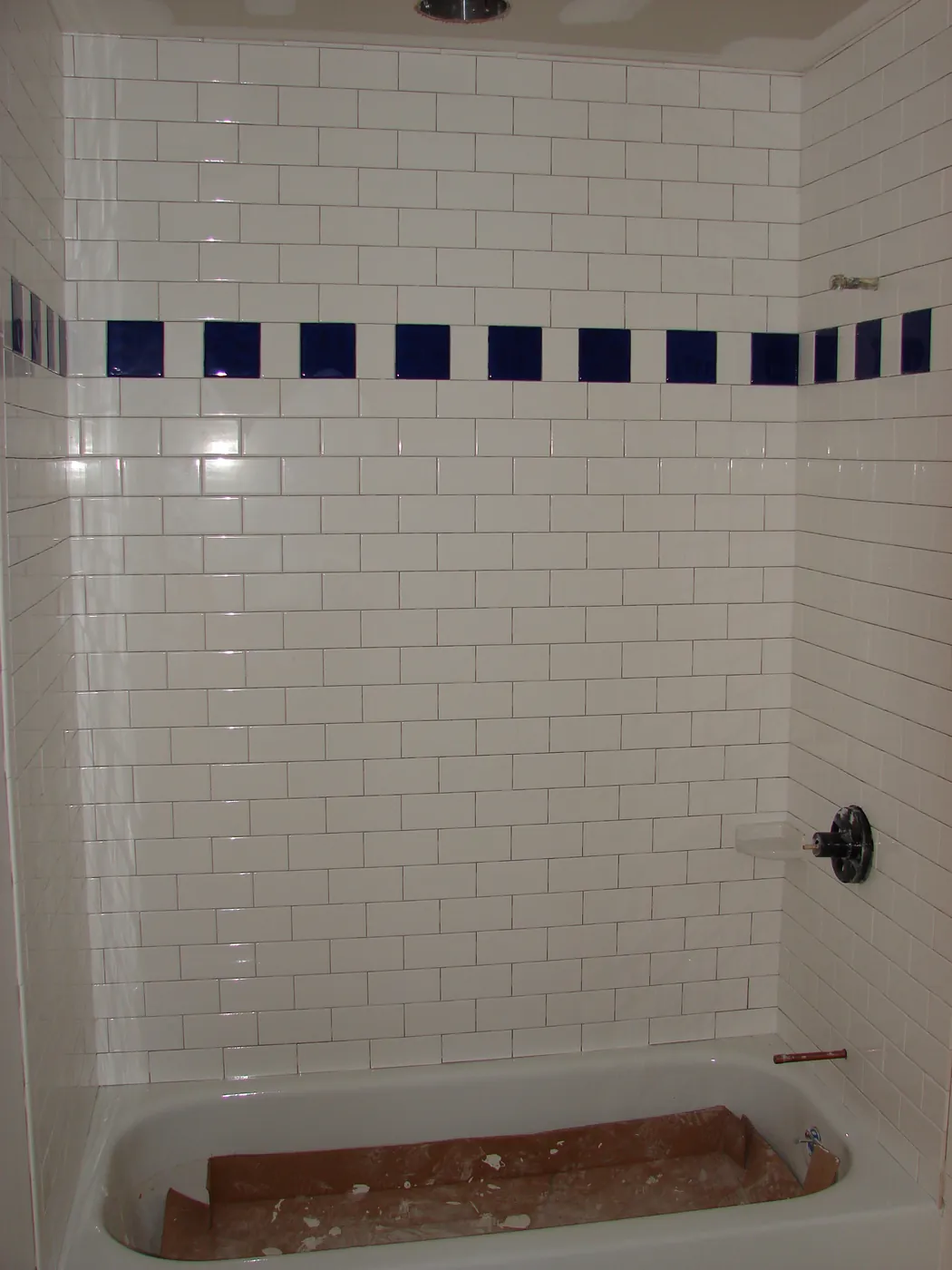 White subway-tile tub-and-shower surround with blue tile accent row and chrome fixture