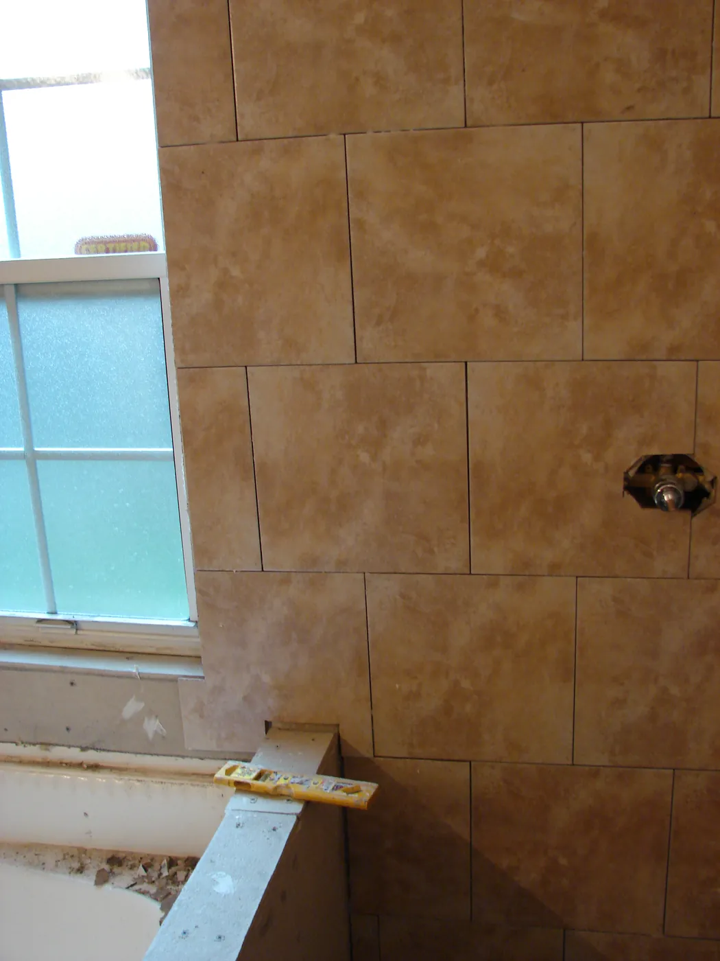 Large-format travertine tiled shower wall beside a glass-block window