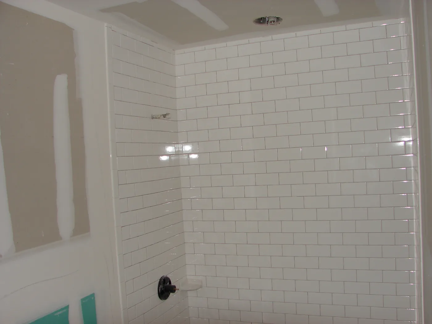 Glossy white subway-tile shower wall with recessed valve