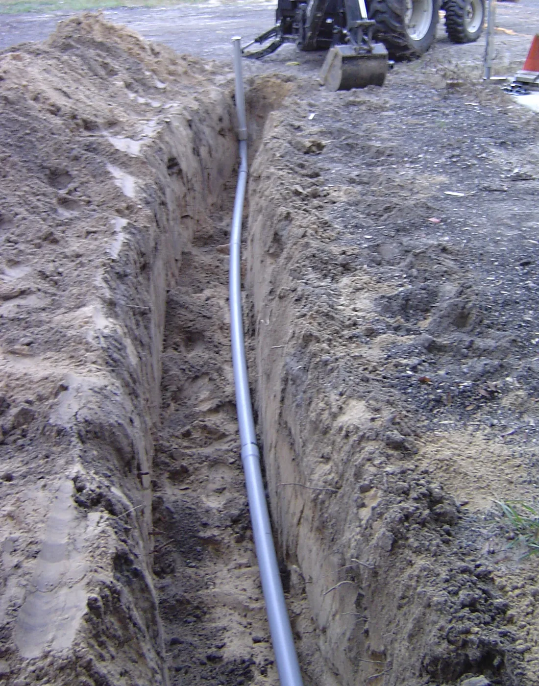 Backhoe tractor digging a trench across a cleared dirt lot with excavated soil pile